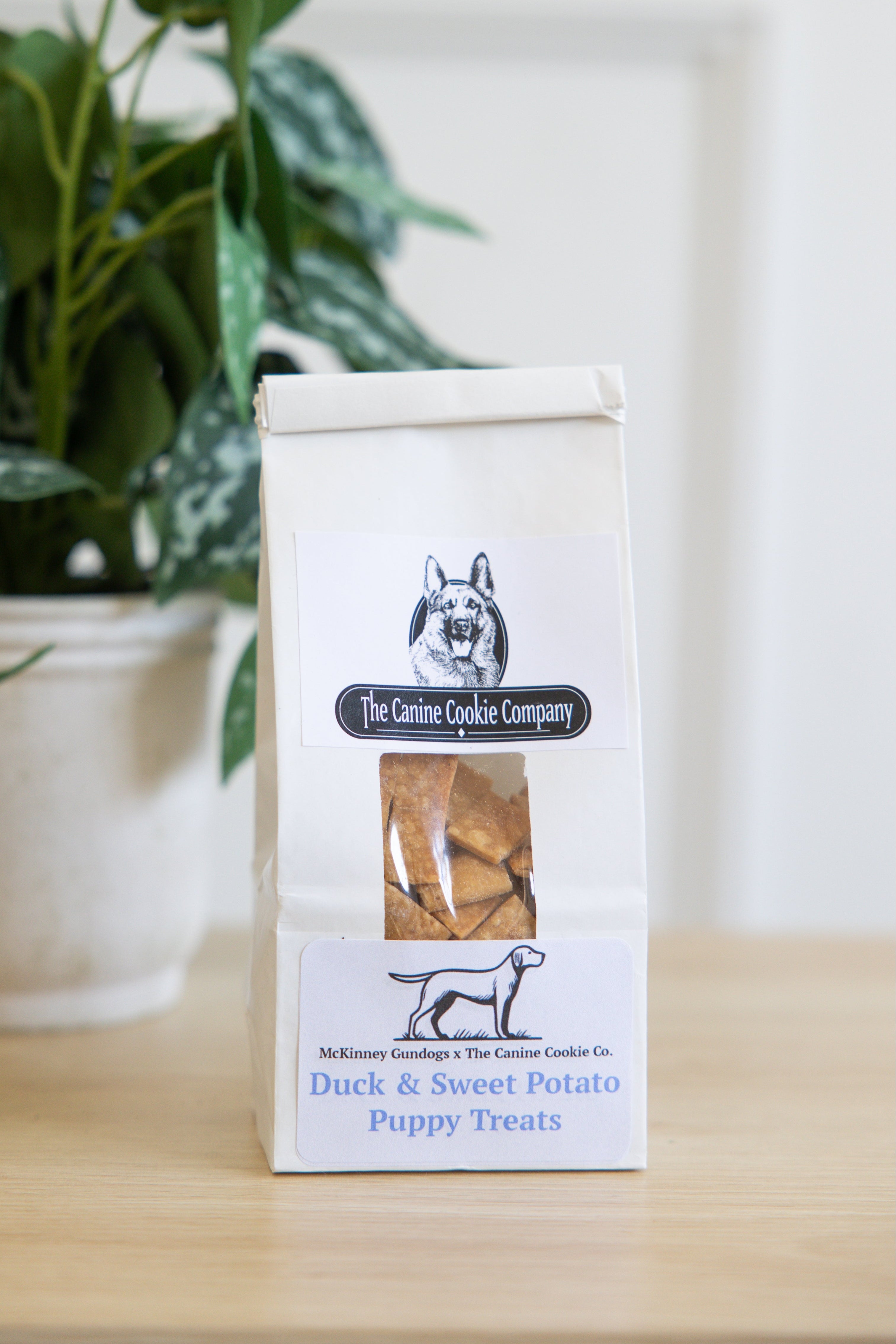 Box of duck and sweet potato puppy treats on a table with a plant in the background
